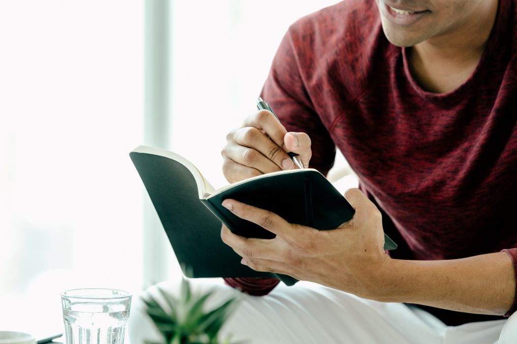 man writing in a book while sitting
